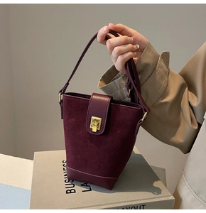 Detail view of burgundy bucket bag with suede and leather textures and gold buckle