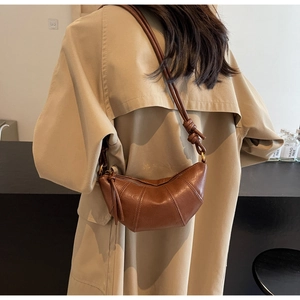 Détail du sac croissant marron avec texture plissée porté sur un trench-coat beige chic