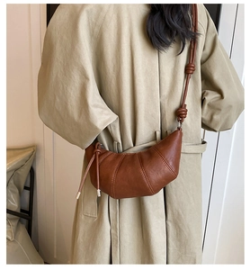 Chic brown leather croissant bag with knotted strap detail worn over a beige coat