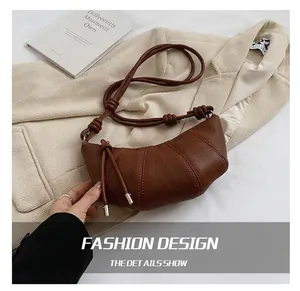 Detail of dark brown leather croissant bag with vertical stitching and knotted shoulder strap