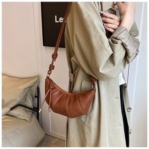 Close-up of brown croissant bag featuring knotted shoulder strap and pleated leather