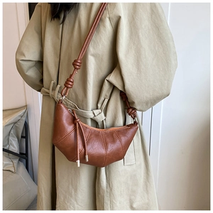 Detail of caramel brown croissant bag with pleated seams on a model in a trench coat