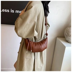 Close-up of brown croissant bag with stitching details and shoulder strap on a trench coat