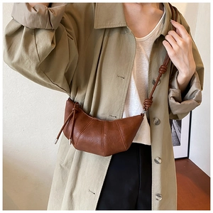 Detailed view of brown croissant bag with pleated seams and knotted shoulder strap detail