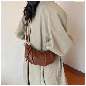 Detail of a brown leather crescent bag with unique knot shoulder strap and vertical stitching