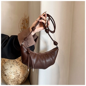 Detail of dark brown leather croissant bag showing knot shoulder strap and stitch textures