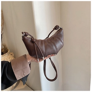 Detail of a dark brown croissant bag with pleated leather texture and a slim shoulder strap