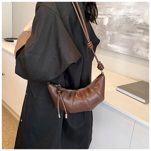 Detail view of a brown croissant bag with stitching and a stylish knotted shoulder strap