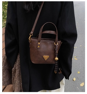 Detail of dark brown faux leather tote with golden hardware and braided pendant