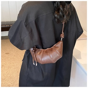 Detail of dark brown crescent bag showing pleated leather texture and knot shoulder strap