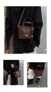 Detail view of a brown vintage tote bag with metal triangle logo and tassel on black coat