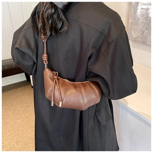 Detail of dark brown leather croissant bag with knotted shoulder strap worn with black coat