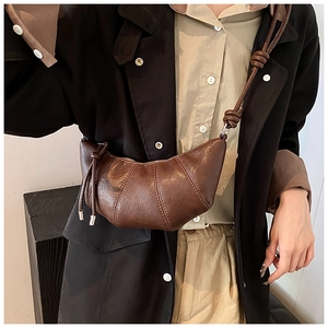 Detail of dark brown croissant bag with segmented stitching and decorative strap knot