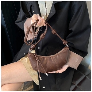 Detail of brown crescent bag featuring pleated faux leather and knotted shoulder strap
