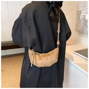 Brown pleated crescent croissant bag shown on a model in a warm stylish home interior