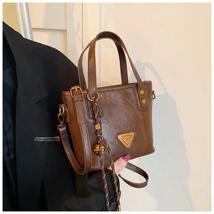 Detail of vintage brown tote bag with metal triangle plaque and braided bell charm