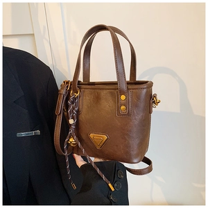 Detailed close-up of dark brown vintage bucket bag with metal logo and woven strap