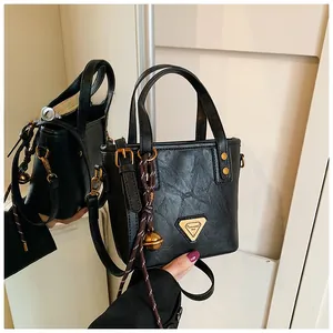 Close-up of black pleated faux leather tote bag with gold triangle logo and bell charm