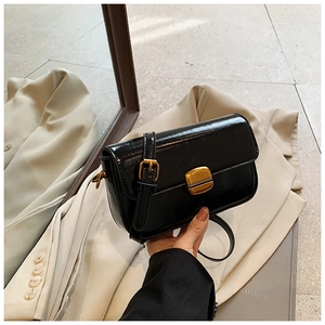 Close-up of glossy black crossbody bag with vintage gold metal clasp and leather texture