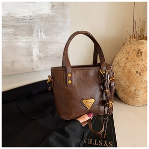Close-up of brown textured leather bucket bag with metallic logo and woven charm detail