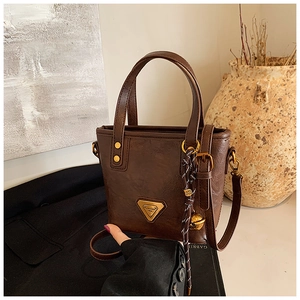 Close-up of deep brown oil wax leather tote with gold emblem and woven pendant charm