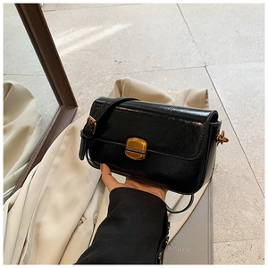 Close-up of black glossy patent leather texture and gold metal buckle on a small square bag