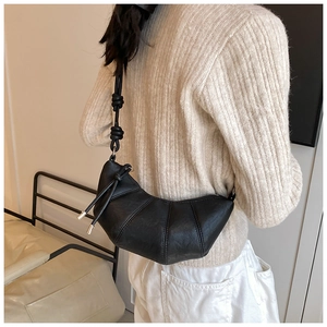 Detail of minimalist black leather croissant bag with knotted strap on a model shoulder