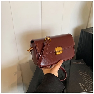 Close-up of a burgundy patent leather flap bag with a golden square clasp and strap