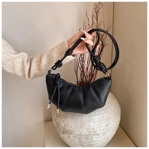 Close-up of black croissant bag with knotted strap and pleated stitching detail