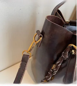 Close-up of golden hardware and woven strap detail on dark brown oil wax leather tote bag