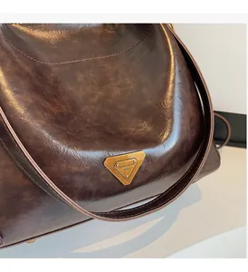 Close-up of deep brown glossy tote bag featuring a vintage bronze triangular metal plaque