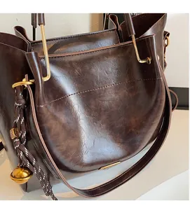 Close-up of brown glossy leather tote with gold U-handle and woven rope charm detail