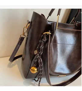 Detail of dark brown faux leather tote bag with gold hardware and woven bell charm