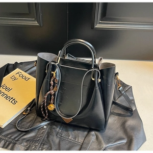 Detailed shot of glossy black tote bag with metal triangle emblem and woven pendant