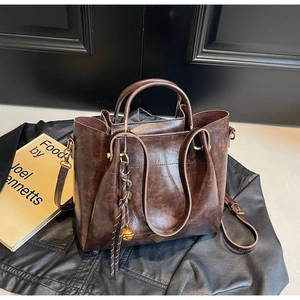 Detail of dark brown vintage tote bag with woven bell charm on a black leather background