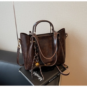 Close-up of vintage brown leather tote bag with braided charm and metal bell detail