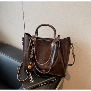 Detail of dark brown oil wax tote bag with gold bell charm and removable strap