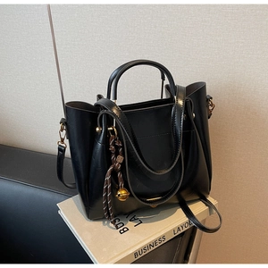Detail of black tote bag with woven rope charm and golden bell on business book prop