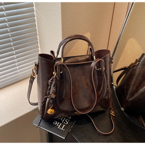 Detail of dark brown retro tote with woven tassel and gold bell on a black surface