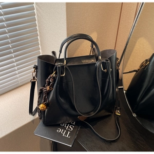 Detail of black faux leather tote featuring metal triangle logo and decorative bell charm