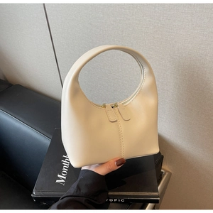 Detailed view of cream white minimalist hobo bag with top metal zipper on a dark book