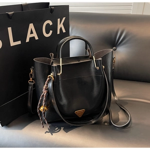 Detail of black tote bag with gold metal logo, leather straps and woven rope pendant