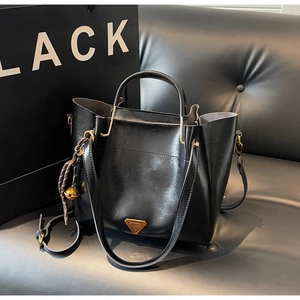 Close-up of black leather tote with golden triangle logo and bell charm on sofa