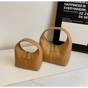 Detail of camel brown leather handbags in two sizes with circular handles and dual zippers