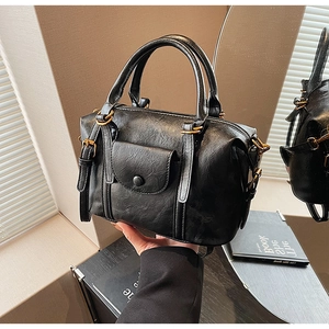 Detailed close-up of a black oil-wax texture Boston bag with gold hardware and front pocket