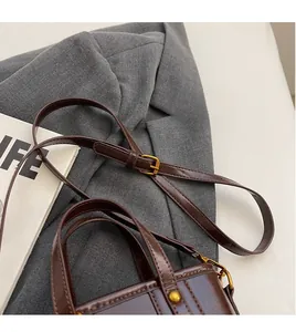 Detail of adjustable long shoulder strap with gold metal buckle on dark brown leather bag
