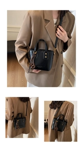 Detail of a black leather bucket bag with gold buckles and a woven ring charm accessory