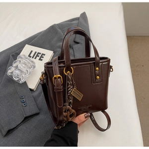 Detailed close-up of a dark brown glossy leather bucket bag with decorative gold charms