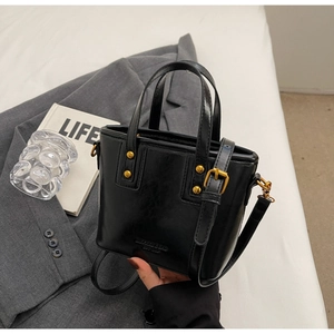 Detail of black polished leather handbag with vintage gold rivets and adjustable strap