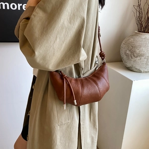 Brown leather croissant bag with pleated texture and knotted shoulder strap in a side view